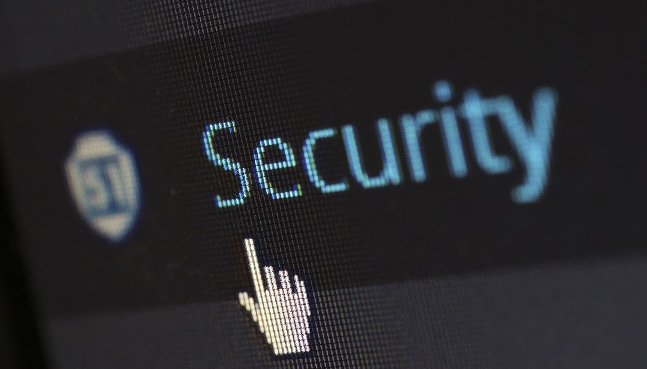 Close-up of a computer screen with the word "Security" in light blue lettering on a dark background. A white, hand-shaped cursor points to the text. A circular blue logo is partially visible on the left.