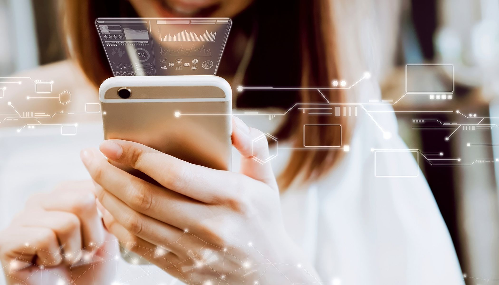Eine Person hält ein Smartphone und blickt auf den Bildschirm. Digitale Oberflächengrafiken und Datenvisualisierungen schweben über dem Gerät und suggerieren Technologie oder Augmented Reality. Der Hintergrund ist unscharf und hebt das Telefon und die Grafiken hervor.